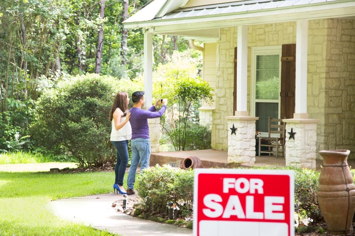 Couple in front of a house for sale.